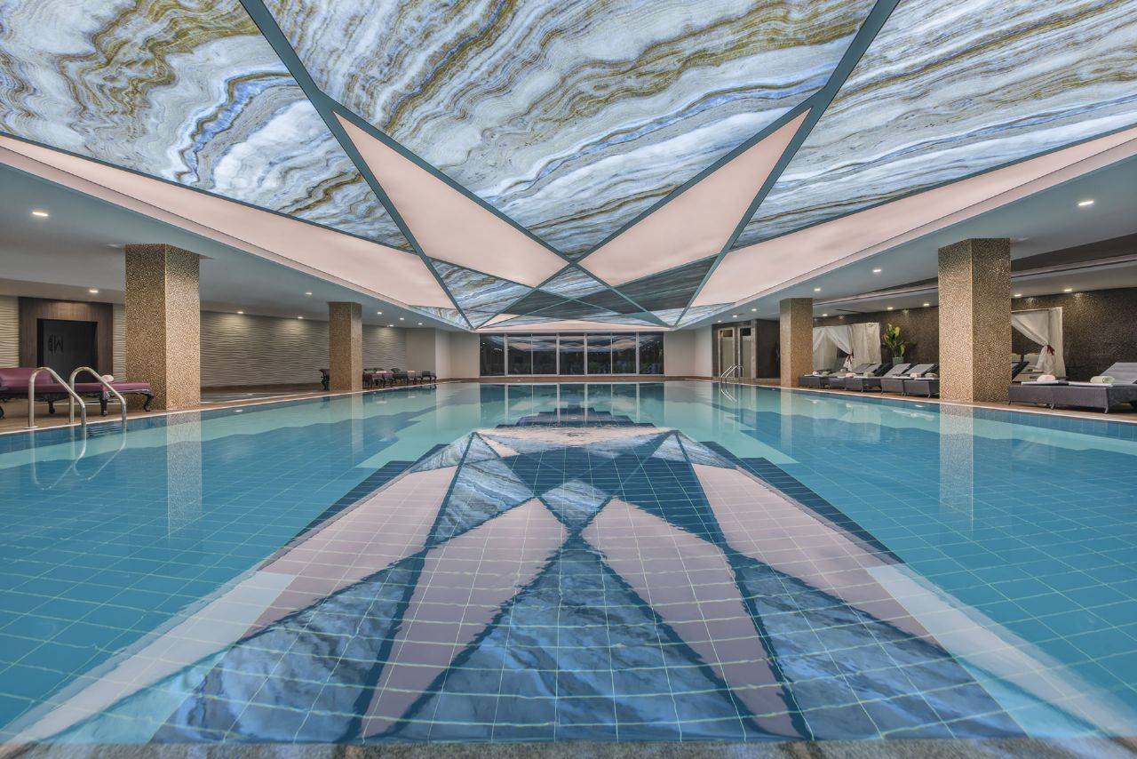 Innenansicht des Delphin BE Grand Resort mit einem modernen Pool und beeindruckender Deckenbeleuchtung.