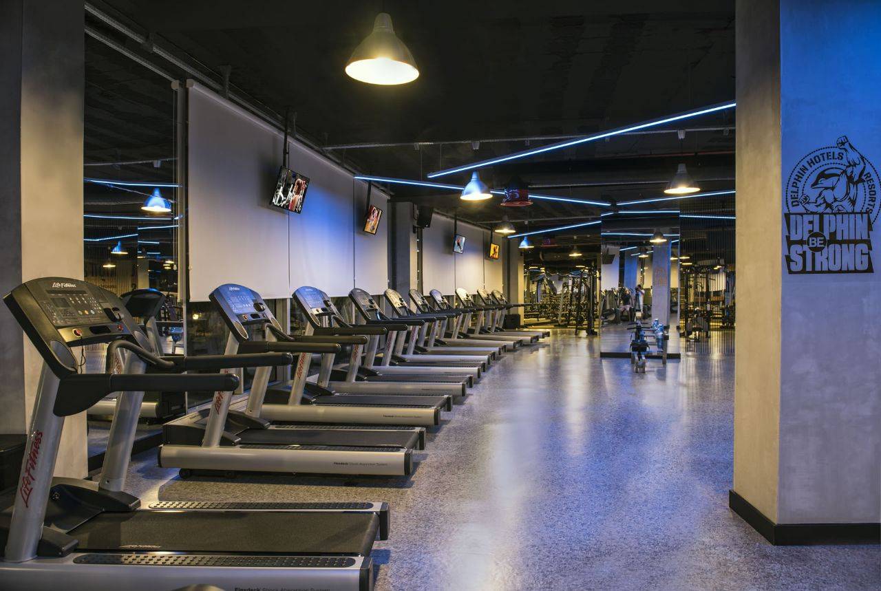 Fitnessraum im Delphin BE Grand Resort mit Laufbändern und moderner Ausstattung in gedämpftem Licht.