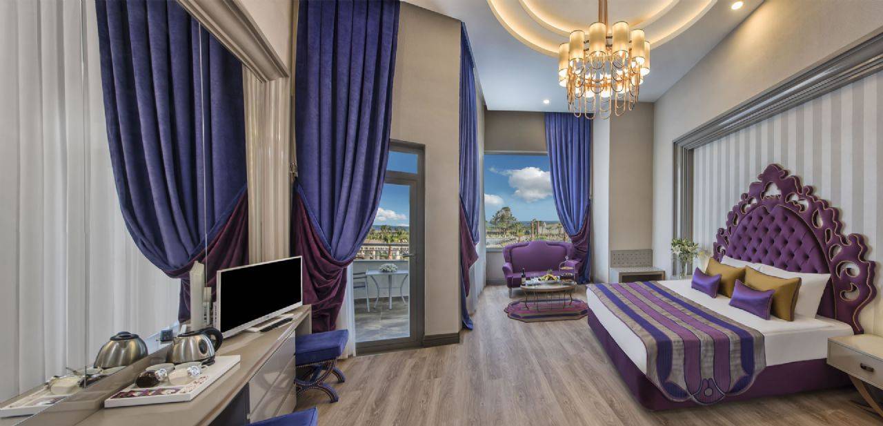 Luxuriöses Zimmer im Delphin BE Grand Resort mit lila Vorhängen, modernem Mobiliar und Blick auf die Landschaft.