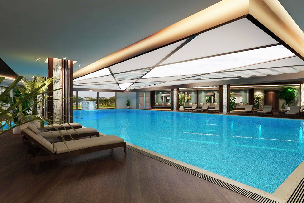 Innenpoolbereich im Delphin BE Grand Resort mit bläulich schimmerndem Wasser und komfortablen Liegen.