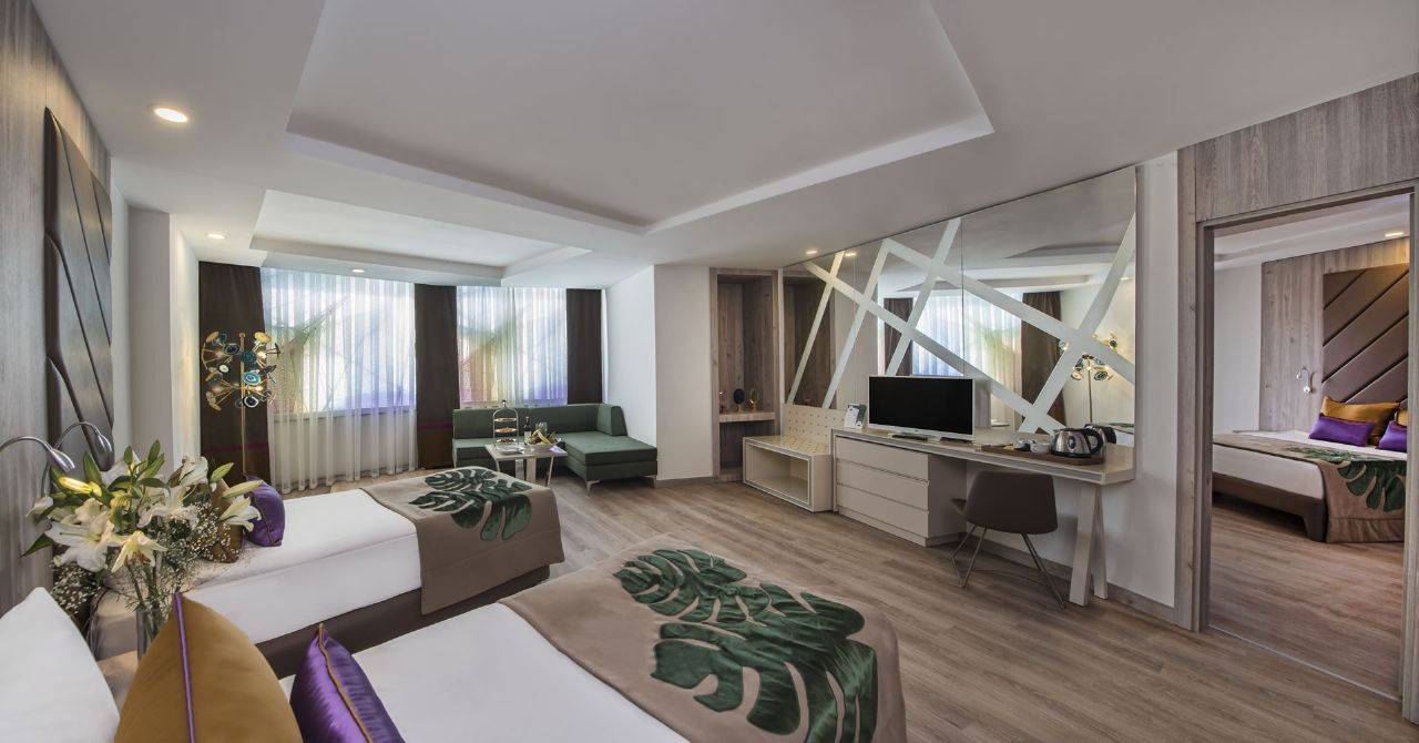 Moderne Zimmer im Delphin BE Grand Resort mit Doppelbetten, Fernseher und Wohnbereich.