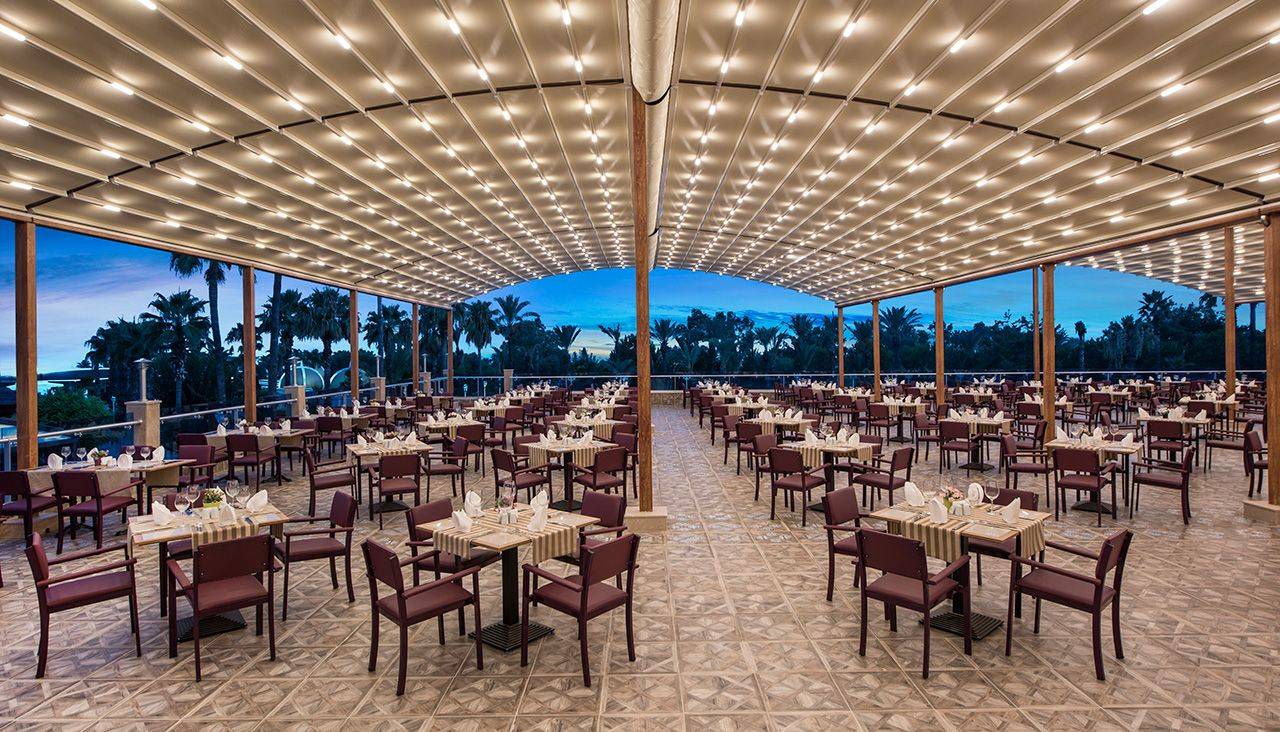 Geräumiges Restaurant des Delphin BE Grand Resort mit eleganten Tischen und schöner Beleuchtung im Freien.