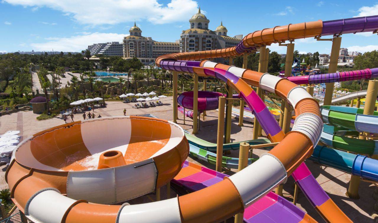 Blick auf die bunten Wasserrutschen im Delphin BE Grand Resort mit Pool und Liegen im Hintergrund.