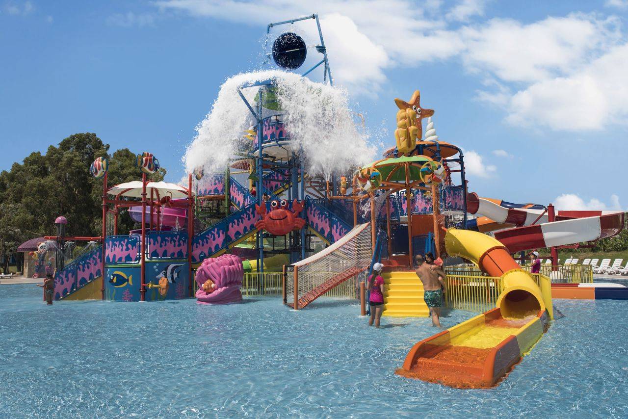 Wasserrutschen und Spielbereich für Kinder im Delphin BE Grand Resort, umgeben von klarem Wasser und sonnigem Himmel.