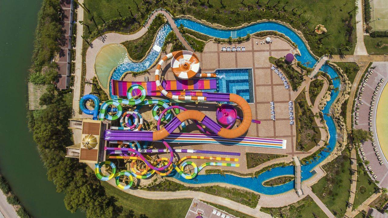 Aussicht auf die farbenfrohen Wasserrutschen des Delphin BE Grand Resort mit Schwimmbädern und Grünflächen.