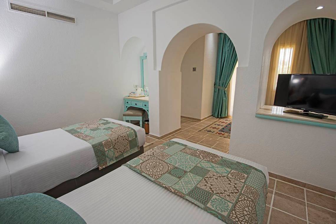 Zwei Betten im Zimmer im Sunrise Royal Makadi Resort mit türkisen Vorhängen und Fernseher.