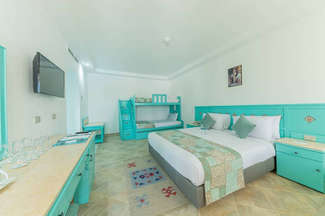 Innenansicht eines Zimmers im Sunrise Royal Makadi Resort mit einem Doppelbett, zwei Etagenbetten und einer Fernsehwand.