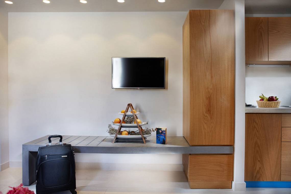 Wohnzimmer von Anna's House mit Fernseher an der Wand, Tisch mit Früchten und Tasche.