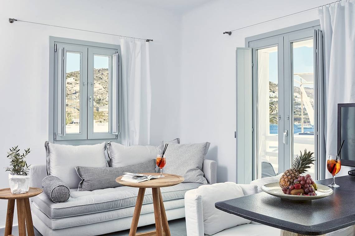 Innenansicht des Wohnzimmers im Mykonos Ammos Hotel mit Couch, Tisch und Ausblick aufs Meer.
