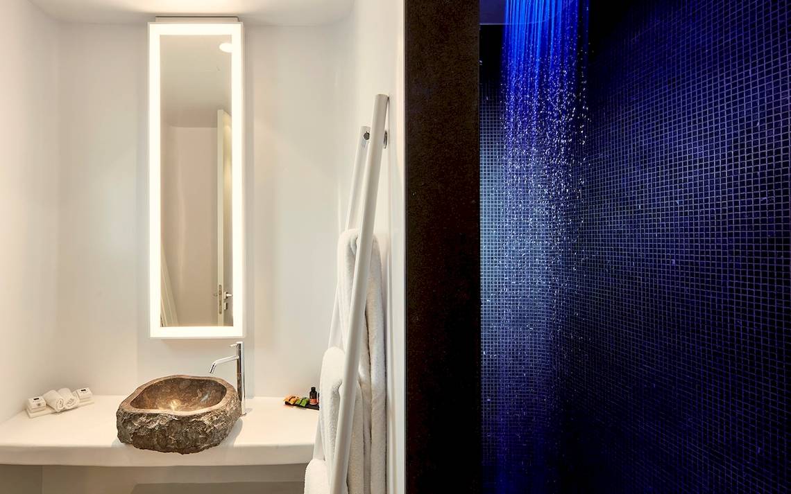Badezimmer im Mykonos Ammos Hotel mit Steinwaschbecken, Spiegel und blauer Regendusche