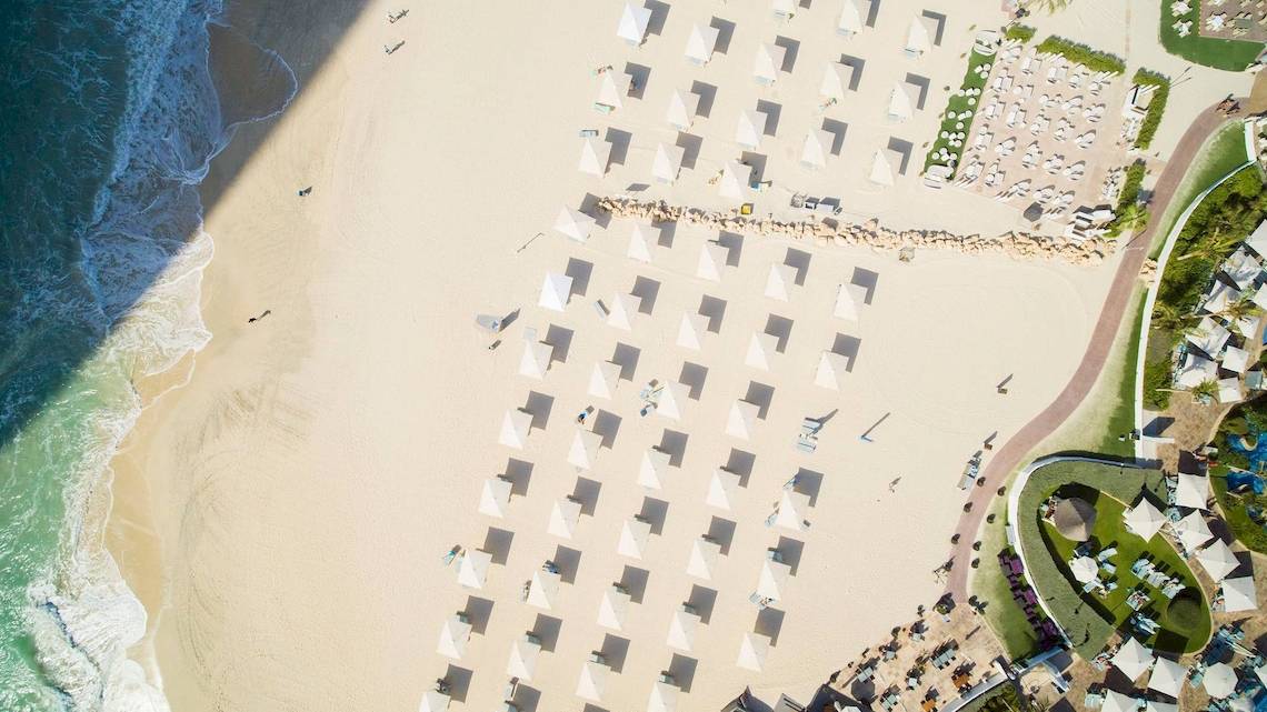 Luftaufnahme des Jumeirah Mina A'Salam Strandes mit vielen weißen Sonnenschirmen und Gästen.