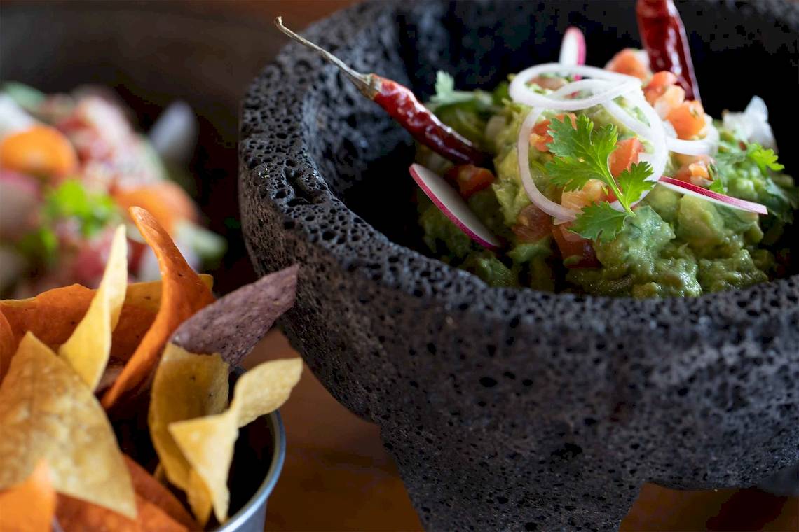 Nahrungsmittel in einem schwarzen Steinmörser mit Tortilla-Chips als Beilage.