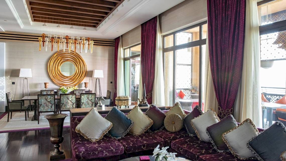 Wohnzimmer des Jumeirah Mina A'Salam Hotels mit einem großen Sofa, vielen Kissen, Esstisch und Stühlen.
