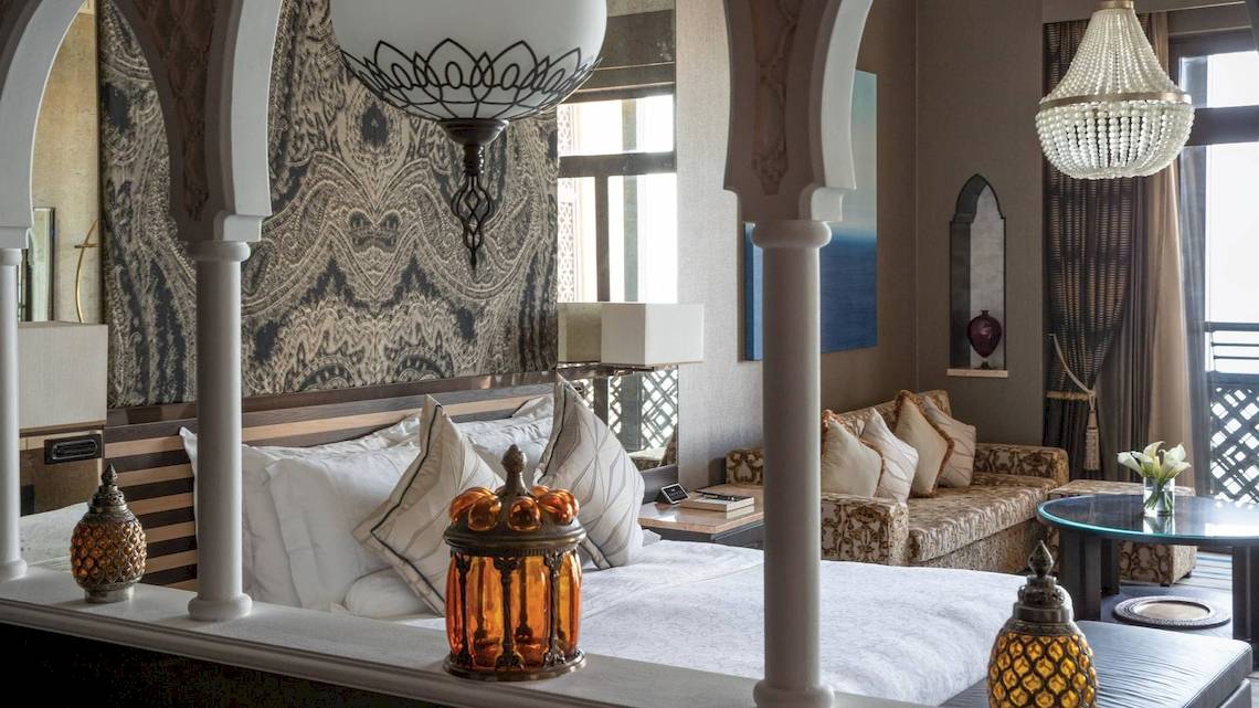 Luxuriöses Hotelzimmer im Jumeirah Mina A'Salam mit üppigen Kissen, eleganten Kronleuchtern und einem Blick auf das Meer.