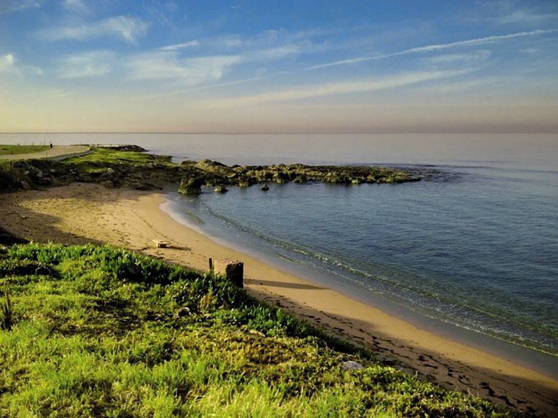 Strandkueste mit gras und felsbrocken vor dem amphora hotel und suites