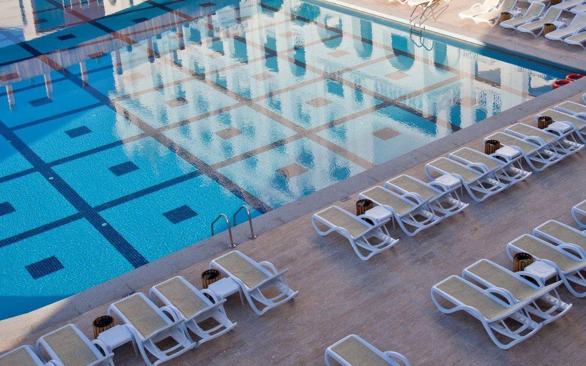 Ein Swimmingpool des Oz Hotels Side Premium mit weißen Liegestühlen und blauem Wasser.