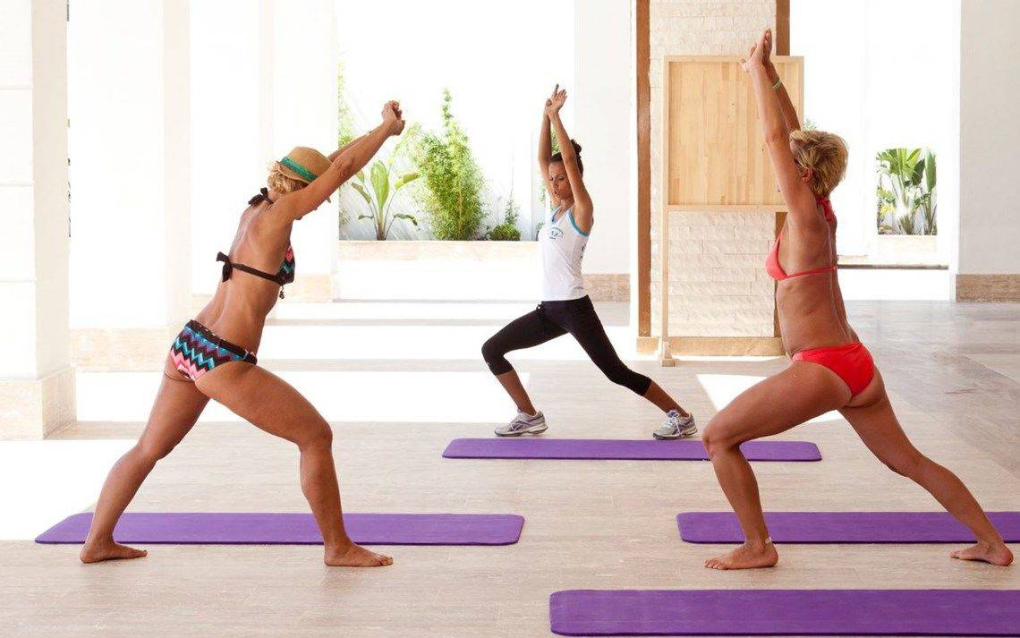 Frauen nehmen an einem Yoga-Kurs im Oz Hotels Side Premium teil, sie sind in Badeanzügen gekleidet und üben Yoga-Posen.