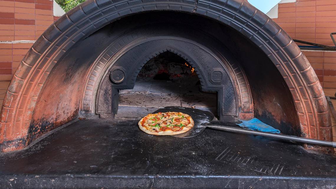 Eine Pizza wird in einem Holzofen des Apollo Beach Hotels gebacken.