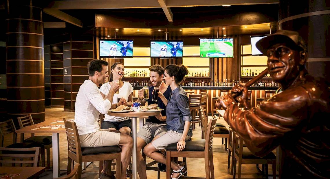 Gruppe von Gästen, die in einem Barbereich des Barcelo Maya Grand Resort Hotels sitzen und essen.