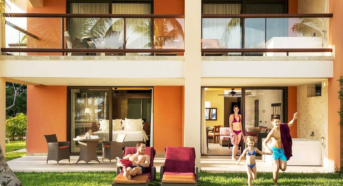 Familie genießt den Außenbereich des Barcelo Maya Grand Resort mit Balkon, Liegestühlen und Spielplatz