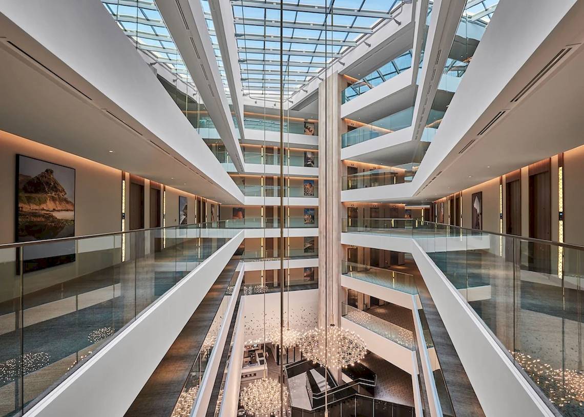 Innenansicht des Mysk Al Mouj Hotels mit Atrium, mehreren Ebenen und großen Glasfenstern.