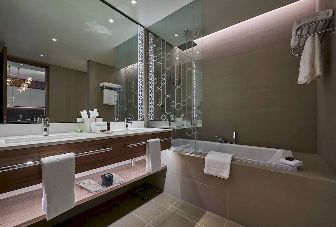 Modernes Badezimmer im Mysk Al Mouj Hotel mit Doppelwaschbecken, Badewanne und Dusche.