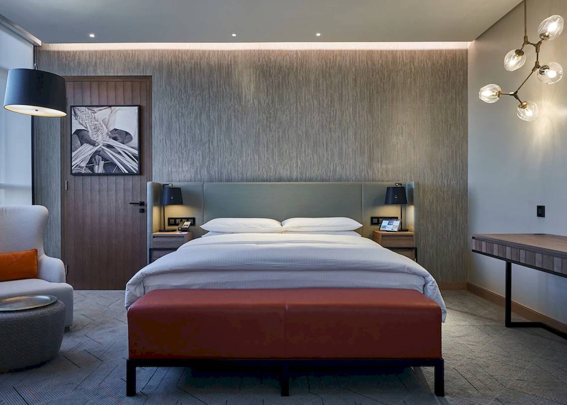 Schlafzimmer im Mysk Al Mouj Hotel mit einem großen Bett, roten Kissen und Holzmöbeln.