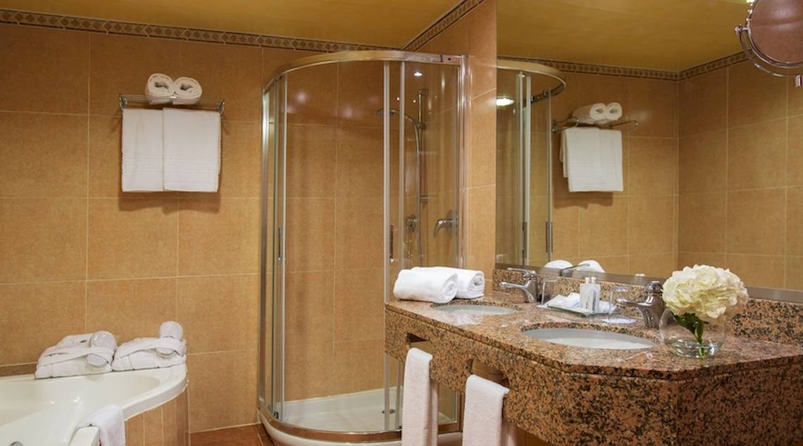 Badezimmer im Universal Hotel Neptuno mit Badewanne, Glasdusche und Waschbecken.