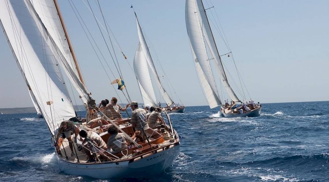 Mehrere Segelboote segeln auf dem Meer mit weißen Segeln unter einem blauen Himmel.