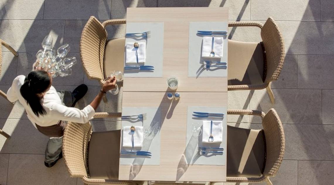 Ein Kellner bereitet einen Tisch im Freien im Universal Hotel Neptuno vor.