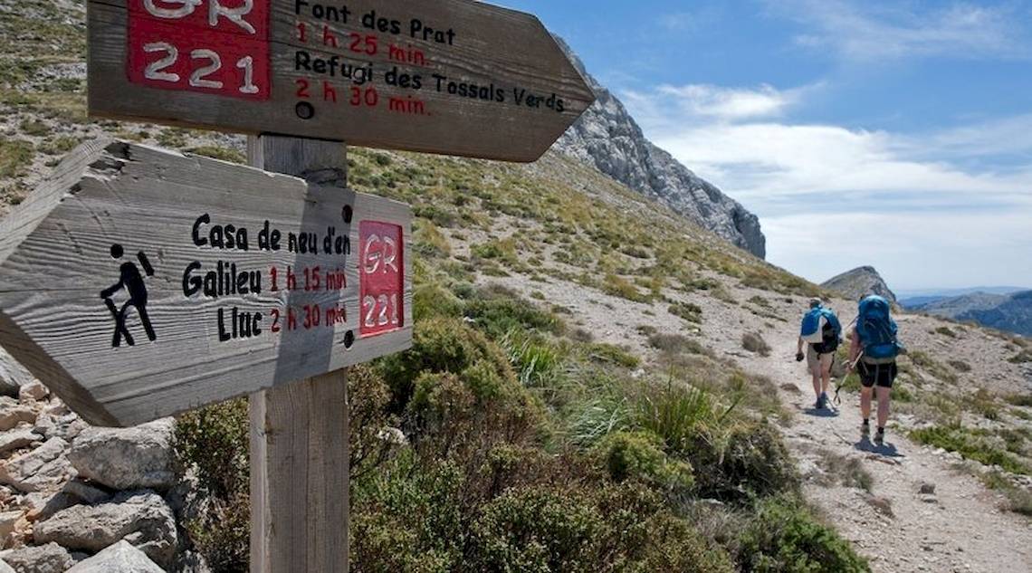 Wanderer auf einem Bergpfad mit einem Wegweiser, der Casa de neu den Gallieu und Lluc anzeigt