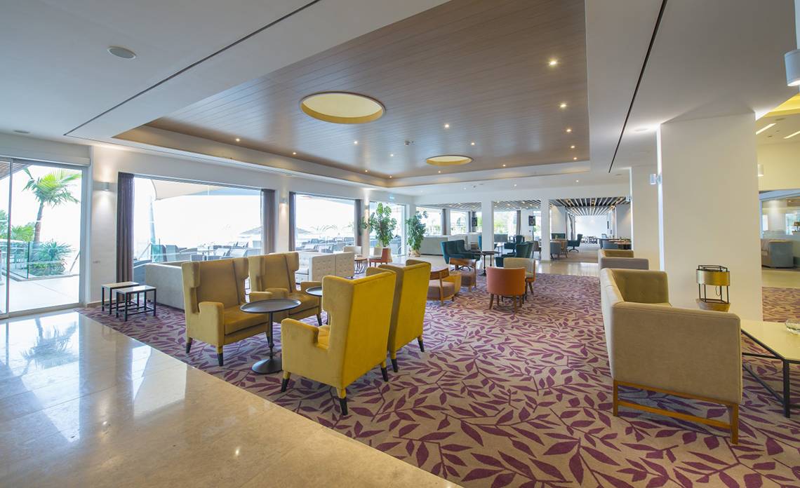 Lobby des Royal Apollonia Beach Hotels mit modernen Möbeln und Panoramafenstern.