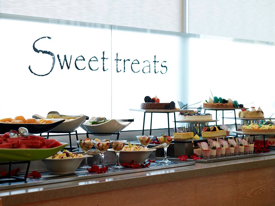 Buffet mit süßen Häppchen im Royal Apollonia Beach Hotel, darunter Kuchen, Obst und Desserts.