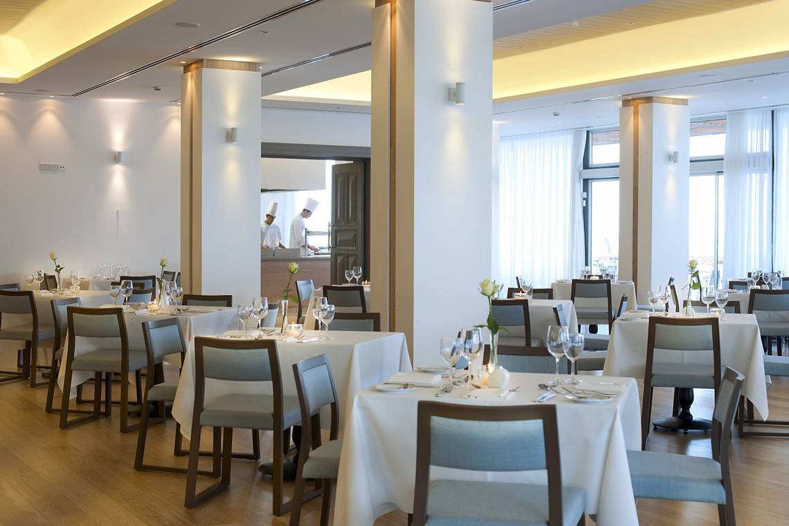 Innenansicht des Restaurants im Royal Apollonia Beach Hotel mit gedeckten Tischen und Stühlen.