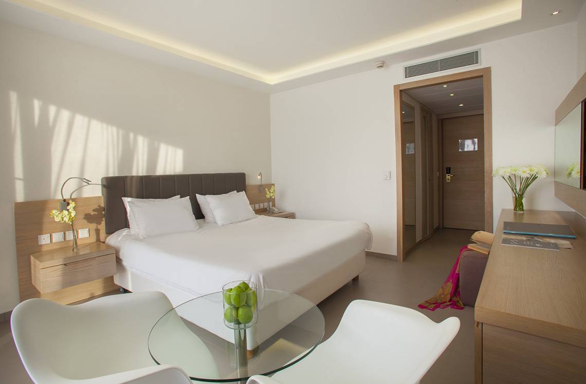 Weißes Zimmer im Royal Apollonia Beach Hotel mit Doppelbett, Tisch und Stühlen.
