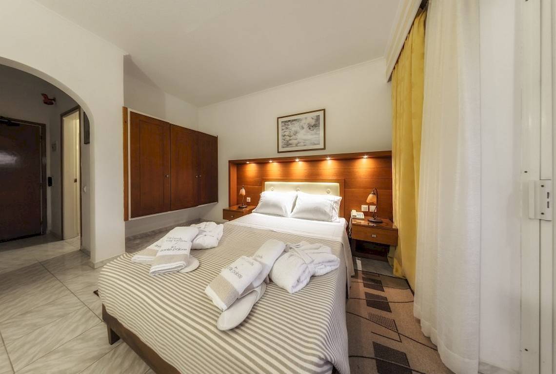 Ein Schlafzimmer im Zante Palace Hotel mit einem Doppelbett, weichen Bettdecken, und hölzerne Nachttische.