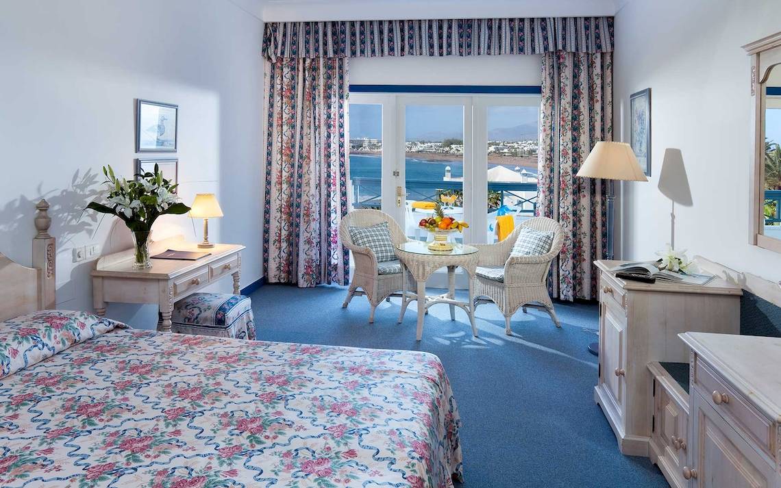Zimmer im Seaside Los Jameos Hotel mit Meerblick, Blumenvase, Schreibtisch und zwei Rattanstühlen.