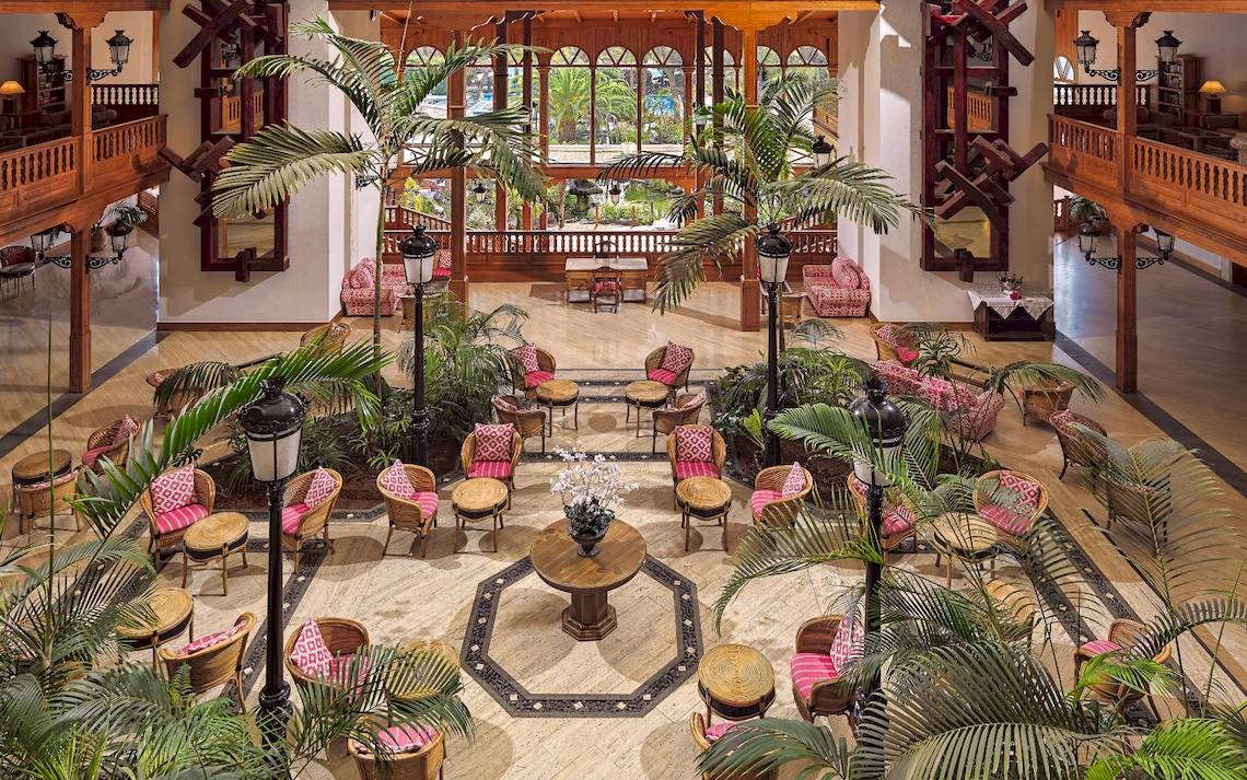 Foyer des Seaside Los Jameos Hotels mit Sofas, Tischen, Palmen und hohen Holzbalkonen.