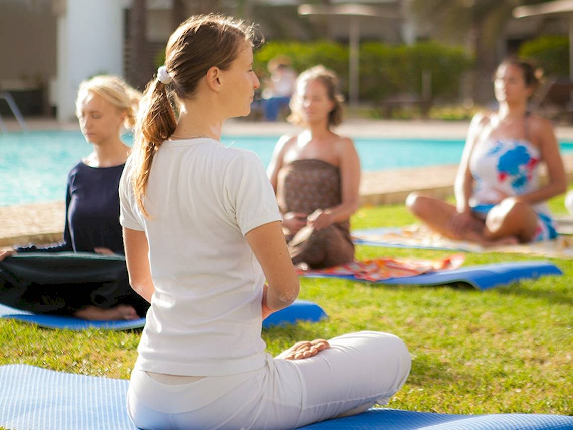 Frauen machen Yoga im Dunas De Sal Hotel vor einem Swimmingpool.