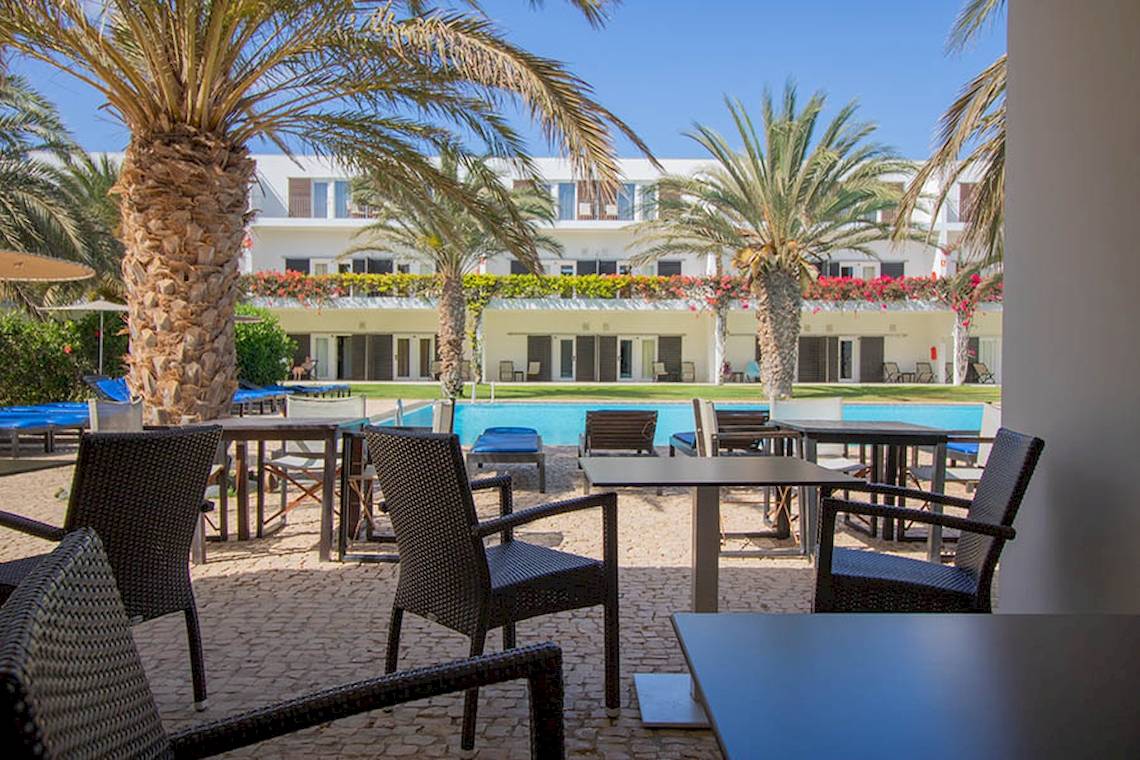 Außenbereich des Dunas De Sal Hotels mit Palmen, Tischen, Stühlen und einem Pool.