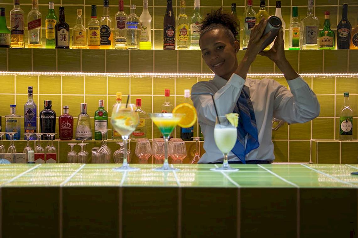 Ein Barkeeper im Dunas De Sal Hotel bereitet Cocktails zu, drei Gläser mit verschiedenen Getränken stehen auf der grünen Theke.
