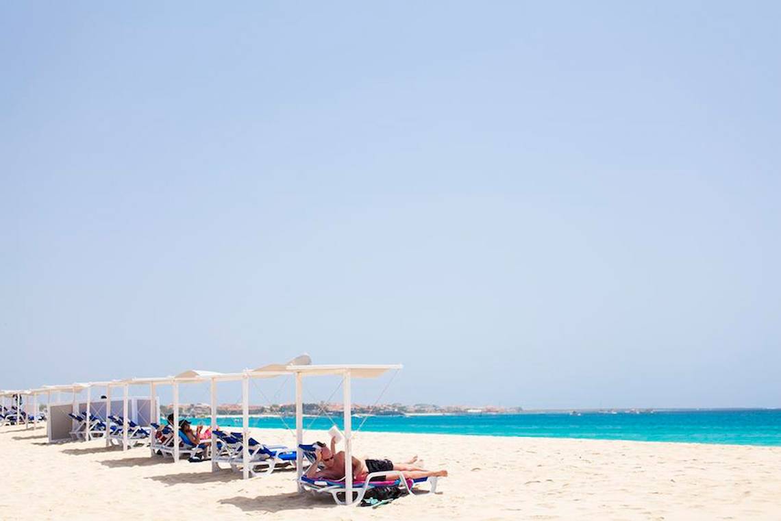 Personen entspannen auf Sonnenliegen am Strand des Dunas De Sal Hotels.