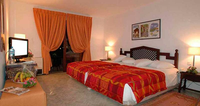 Schlafzimmer im Royal Decameron Issil Resort mit zwei Betten, Tisch, Fernseher und Lampen.