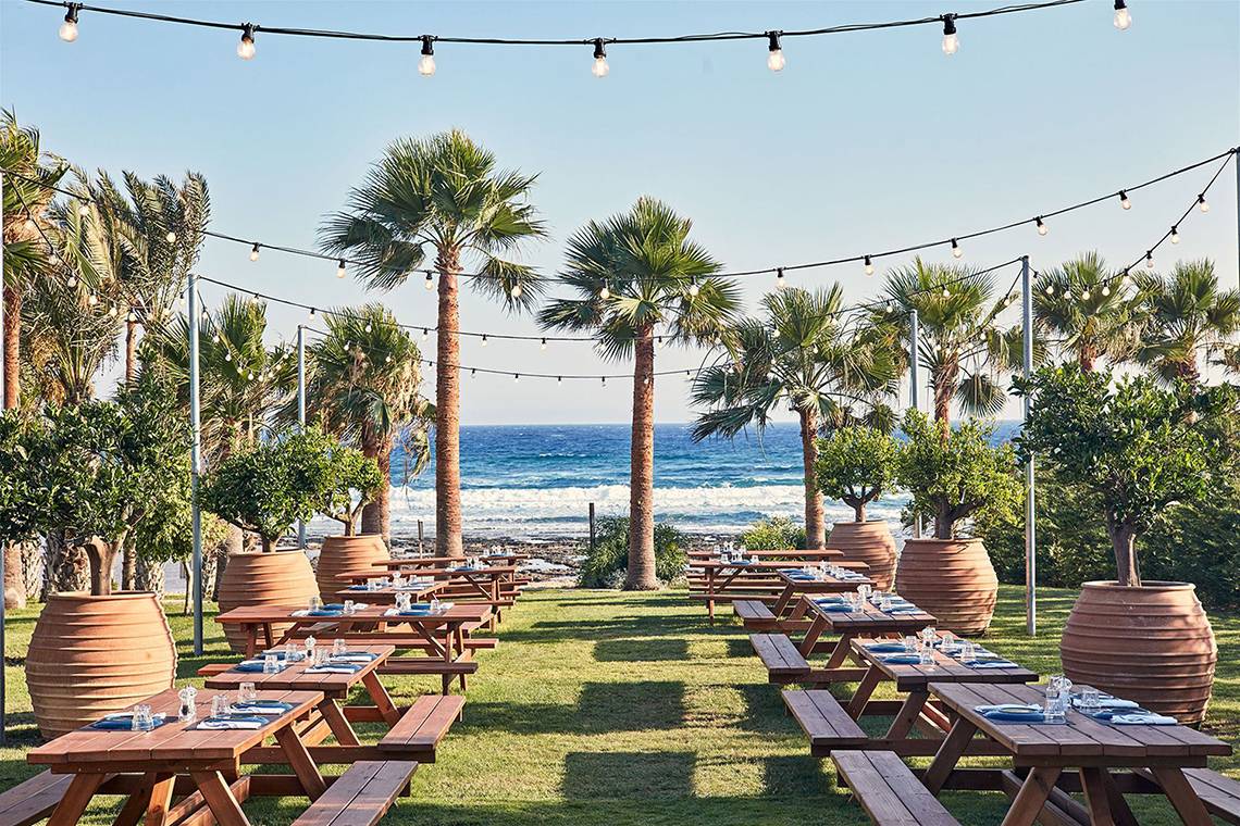 Gartenterrasse des Mare Ayia Napa Hotels mit Blick auf das Meer und abendliche Lichter.