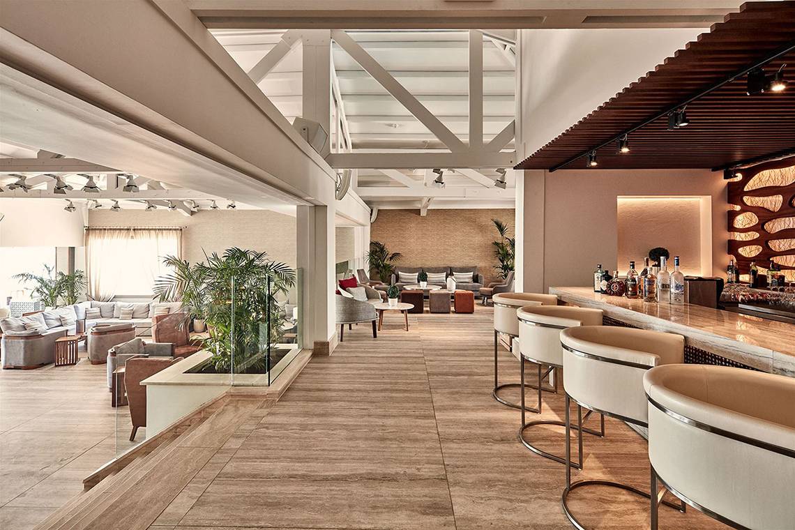 Innenansicht der Bar im Mare Ayia Napa Hotel mit Holzboden, modernen Stühlen und einer Theke.