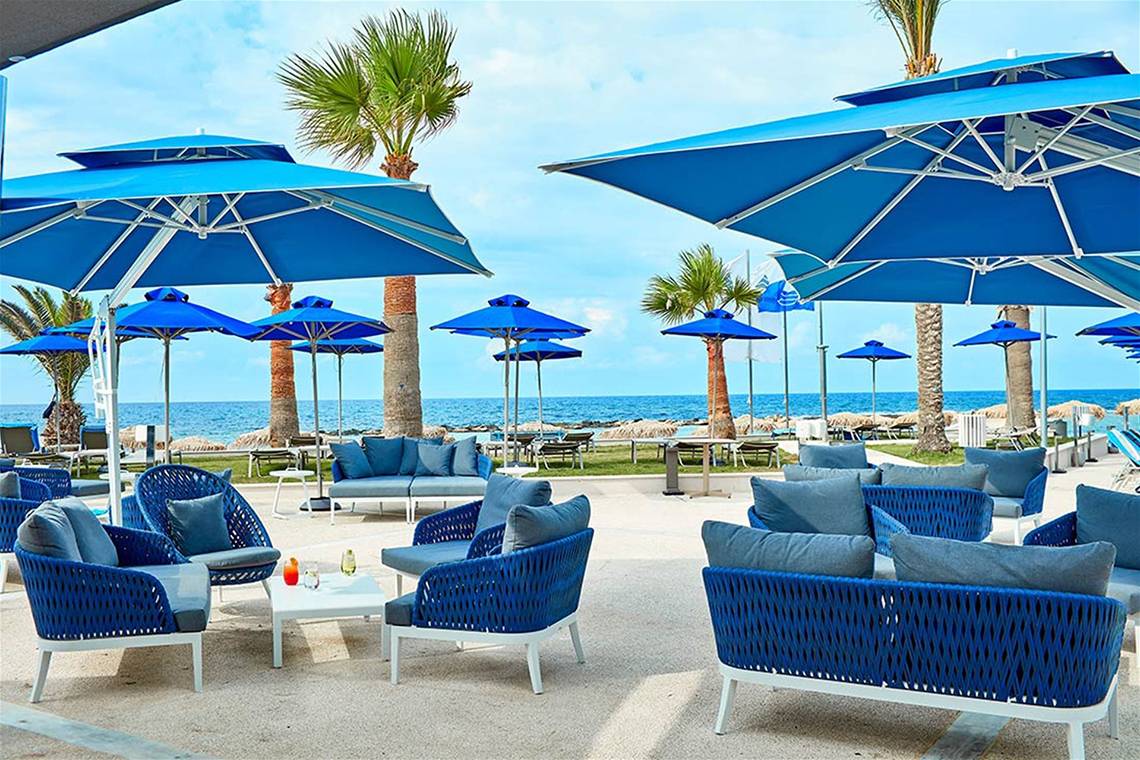 Loungebereich des Mare Ayia Napa Hotels mit blauen Sonnenschirmen und Möbeln am Meer.
