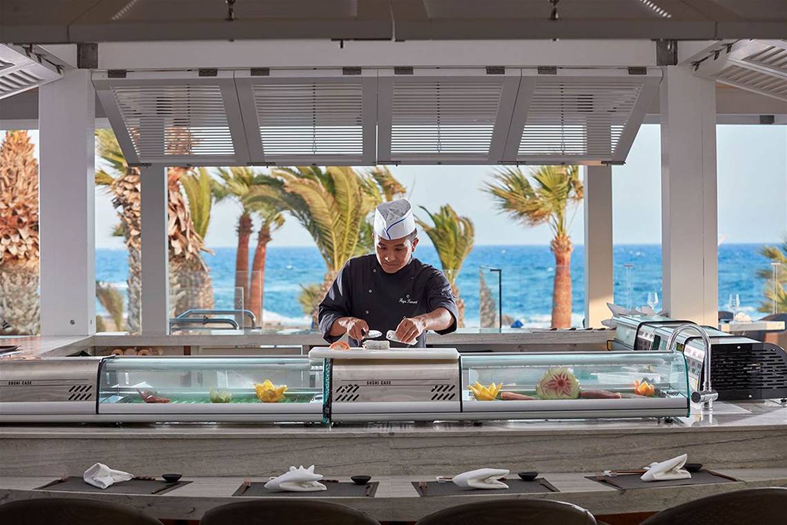 Ein Koch bereitet Sushi in einer Glasfalle im Mare Ayia Napa Hotel zu, mit Blick auf das Meer.