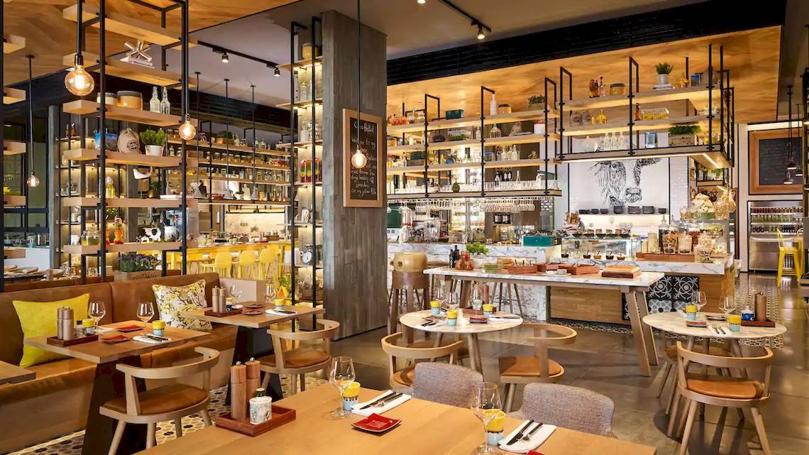 Innenbereich des Grand Hyatt Abu Dhabi Hotel Restaurants mit Holztischen, Stühlen und Regalen voller Flaschen.