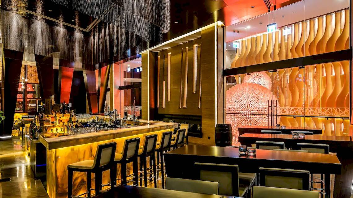 Innenbereich der Bar im Grand Hyatt Abu Dhabi Hotel mit goldenem Tresen und modernen Möbeln.