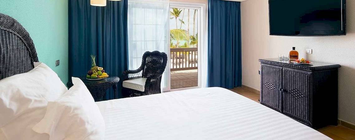 Hotelzimmer im Barcelo Bavaro Beach mit Bett, Früchten auf dem Tisch und offenem Balkon.